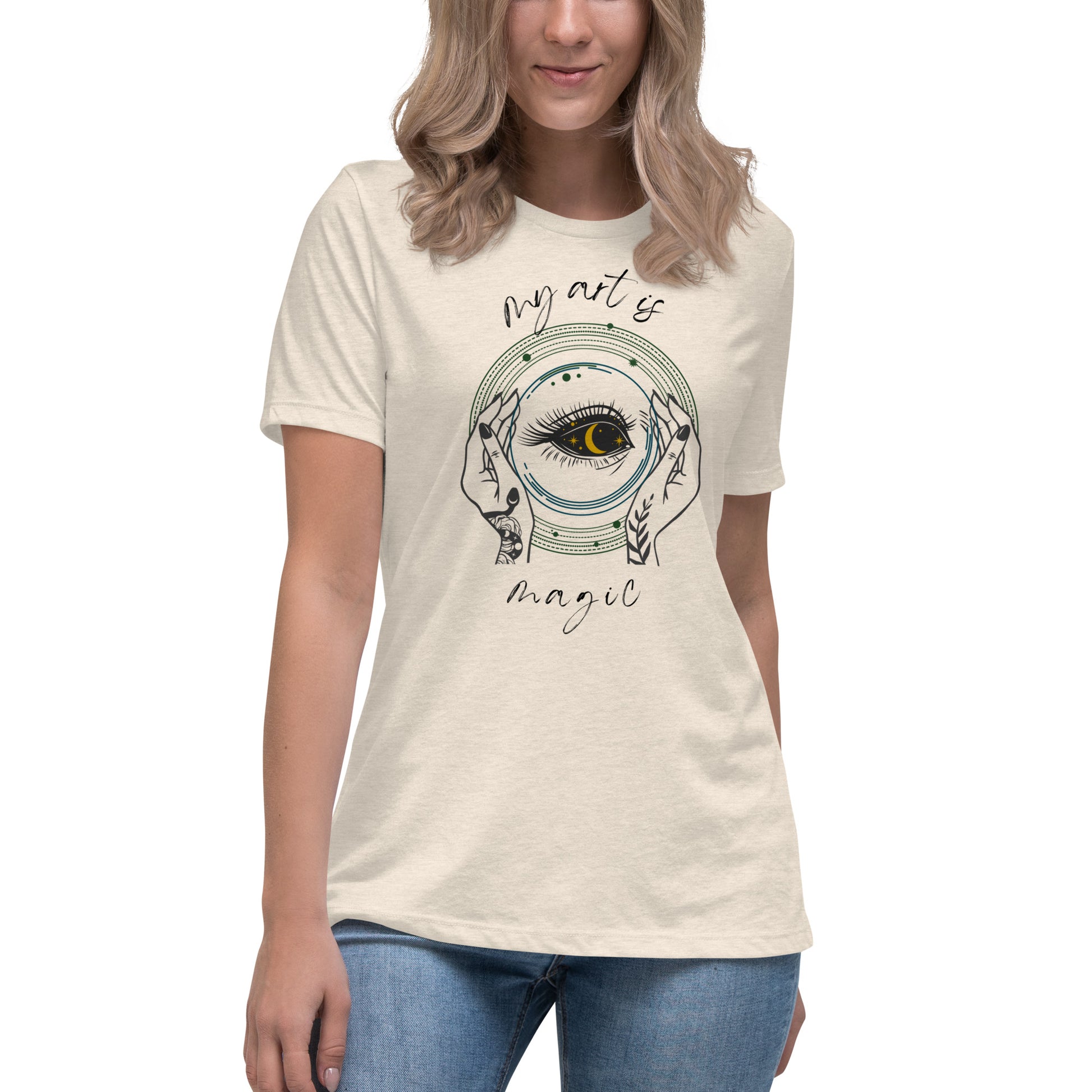 Close up of My Art is Magic T-shirt with heather stone natural colored background and witchy hands with a long lashed eye with a crescent moon as pupil. 
